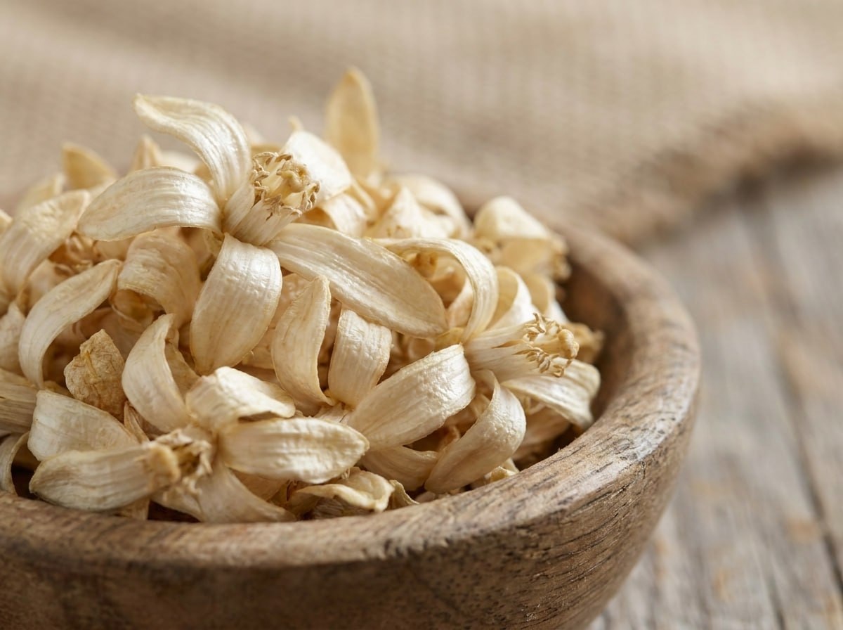 Close-up of dried orange blossom flowers in a wooden bowl, soft natural light showing their pale cream color and delicate texture