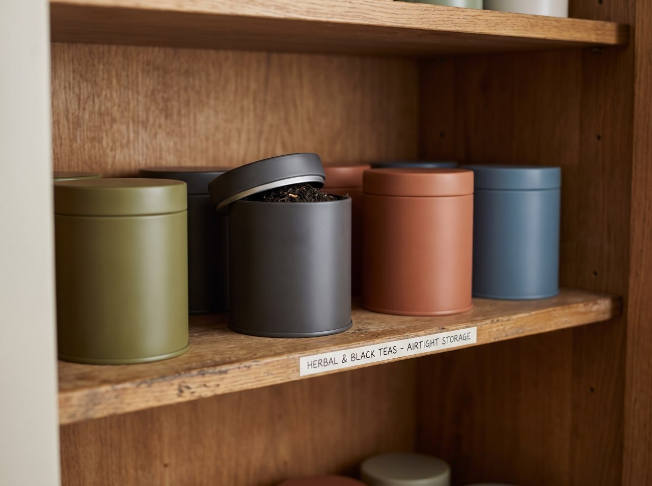 Airtight matte metal tea tins arranged on a wooden shelf