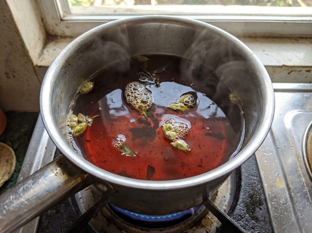 Dark strong black tea boiling in a small pot on a stovetop, steam rising, deep mahogany color